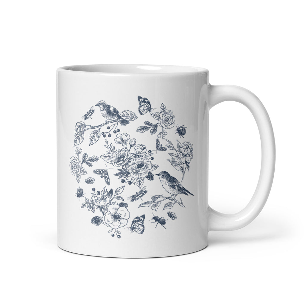 11 ounce white mug with a design in blue featuring a variety of birds, garden plants and insects